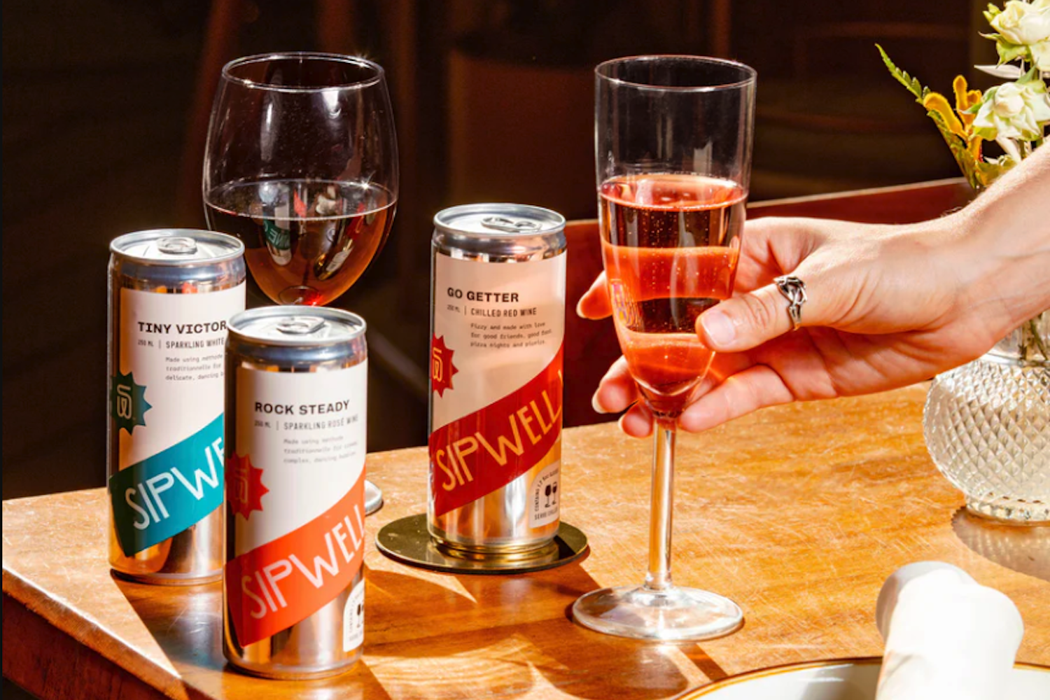 Three cans of wine from Sipwell Wine Co. sit on a table alongside glasses of the wine — sustainable wine